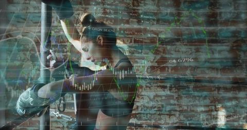 Determined female boxer training in urban industrial gym with stock market chart overlay
