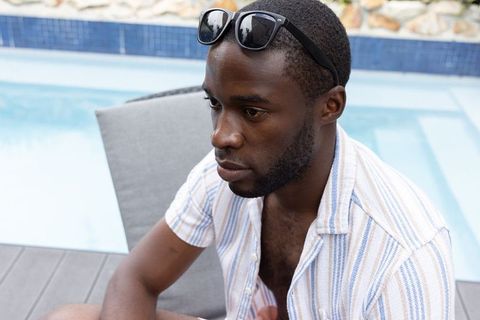 African american man relaxing at pool wearing striped shirt and sunglasses