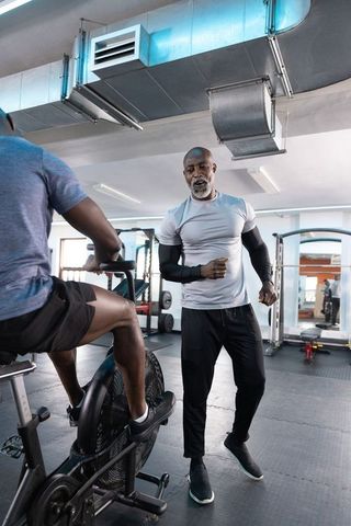 African american trainer guiding male client on air bike in industrial gym