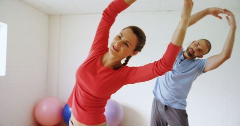 Couple Stretching Together During Yoga Class in Bright Gym