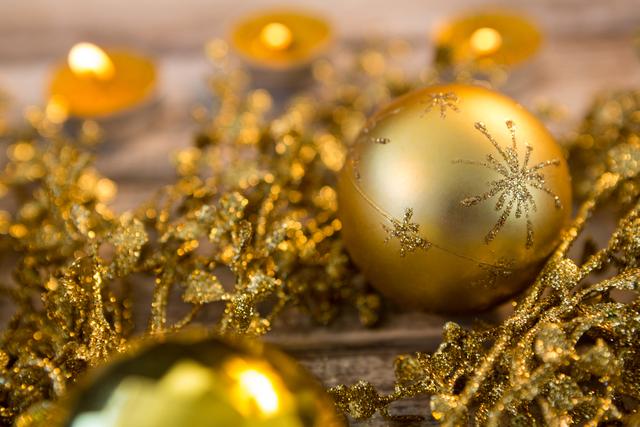 Golden Christmas ornaments and candles create a festive and warm atmosphere on a wooden surface. Ideal for holiday-themed designs, greeting cards, festive advertisements, and seasonal blog posts.