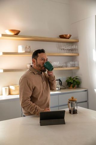 Mature asian man drinking coffee at kitchen island using tablet in modern minimalist home