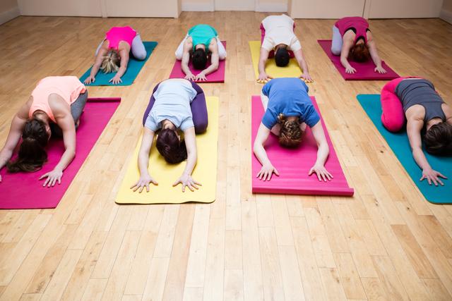 Group of individuals practicing child's pose in a yoga class on colorful mats in a fitness studio. Ideal for promoting wellness, fitness, and group exercise activities. Useful for illustrating yoga classes, fitness routines, and healthy lifestyle concepts.