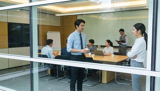 Asian professionals conversing in glass-walled conference room during casual coffee break