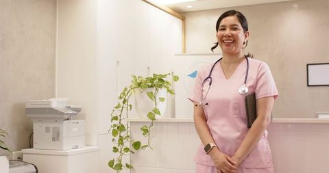 Smiling nurse standing at clinic reception wearing pink scrubs and stethoscope