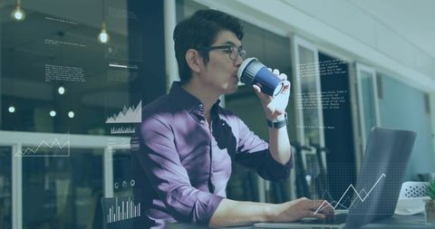 Asian man analyzing data on laptop while sipping coffee in modern coworking space