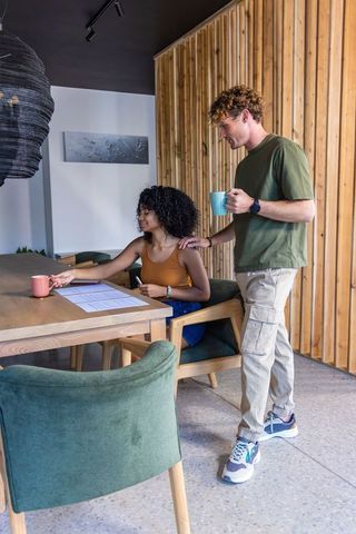 Diverse couple collaborating over documents while drinking coffee in modern coworking space