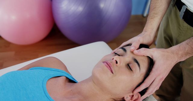 Image shows woman receiving head massage from therapist in wellness center. Useful for promoting spa services, stress relief therapy, wellness practices, massage therapy training, and self-care advertisements.