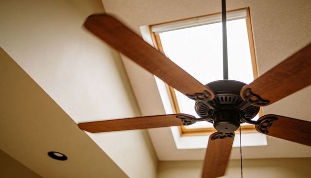 Ceiling fan spinning under skylight with wooden blades bronze decorative scrollwork interior