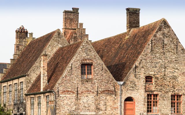 The image features a historic building with an old brick facade and red-tiled roof complemented by multiple chimneys. The rustic and weathered appearance of the structure suggests it is a historically significant site or a well-preserved architectural piece in European urban settings. Ideal for illustrating content on historic architecture, travel magazines, European culture, and educational material about medieval buildings. A suitable choice for backgrounds in presentations and thematic web design involving vintage aesthetics.
