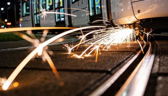 Sparking tram wheel throwing bright orange-white sparks along streetcar rails at night