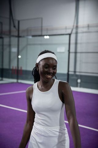 African american female tennis player smiling on purple indoor court wearing white headband