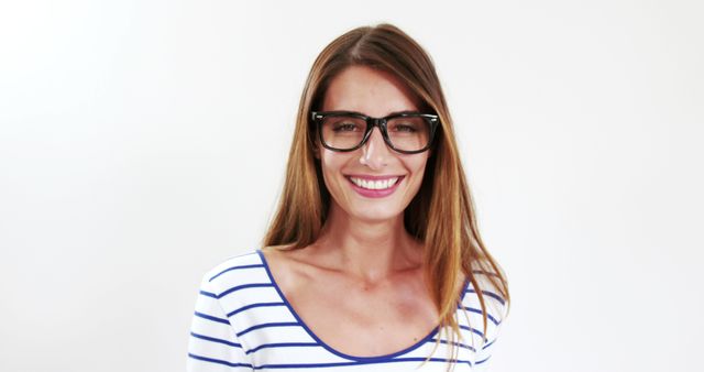 A woman with long hair wearing glasses and a striped shirt, standing against a white background and smiling. Suitable for use in lifestyle and fashion advertisement, articles about eyewear, or content promoting positivity and joy.
