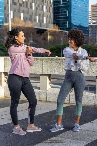 Diverse women stretching and smiling together on urban terrace before outdoor workout
