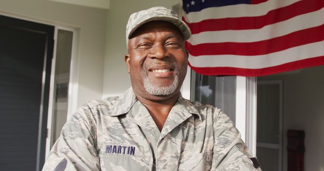 Elderly military veteran proudly standing in uniform in front of an American flag. Ideal for use in promotions of veteran services, Independence Day celebrations, military appreciation campaigns, and features about patriotism and national pride.