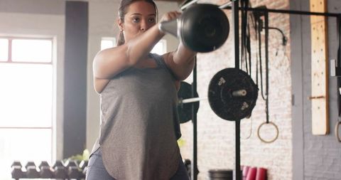 Woman performing kettlebell swing in industrial gym, focused strength training workout