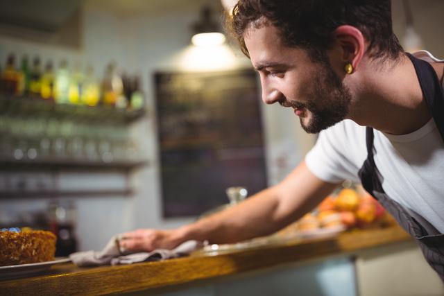 Smiling waiter wiping counter with napkin in cafÃ©