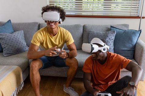 Two friends playing VR games wearing white headsets and holding controllers in living room