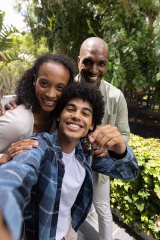 Smiling diverse family taking backyard selfie with teenage son holding sunglasses