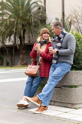Mature couple enjoying coffee on city bench wearing scarves and beanie on overcast day