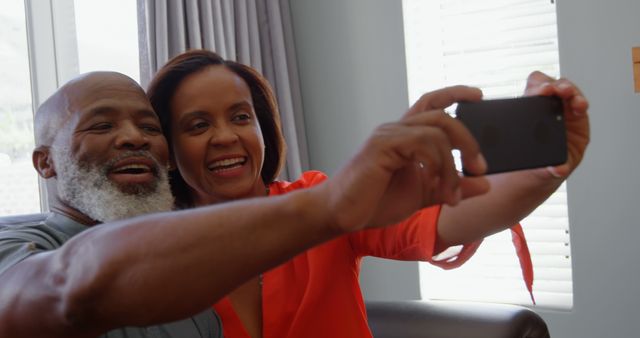 Front view of mature black couple clicking selfie with mobile phone in a comfortable home. They are smiling and posing 4k