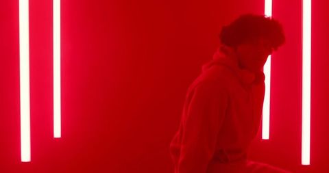 Man with headphones leaning on neon red light wall