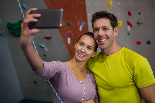 Couple taking selfie at indoor climbing gym, smiling and enjoying their time together. Ideal for promoting fitness, active lifestyle, and sports activities. Suitable for use in advertisements for gyms, fitness clubs, and health-related products.