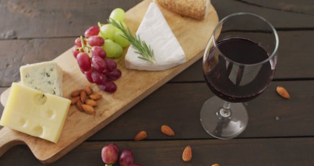 Image of cheeses, bread, grapes and nuts on board and glass of red wine on wooden table. quality light food snack and drink.