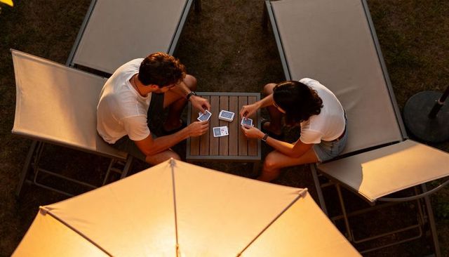Couple playing cards at patio table during golden hour sunset with glowing umbrella light