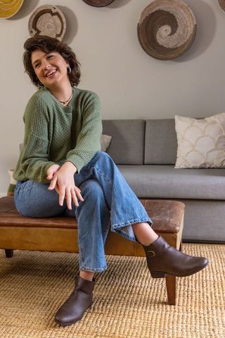 Smiling woman sitting on leather bench in cozy living room wearing green sweater