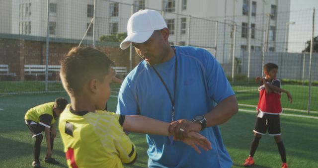 Coach is instructing a young soccer player on a sports field. They appear to be focusing on an arm stretching exercise, emphasizing proper technique. This image can be used to depict sports training, youth mentorship, teamwork, and athletic development in advertisements, educational materials, or sports programs.