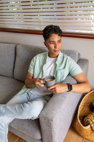 Young Man Relaxing on Sofa with Coffee Mug Wearing Green Shirt