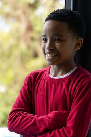 Smiling african american boy standing by window wearing red shirt and white tee