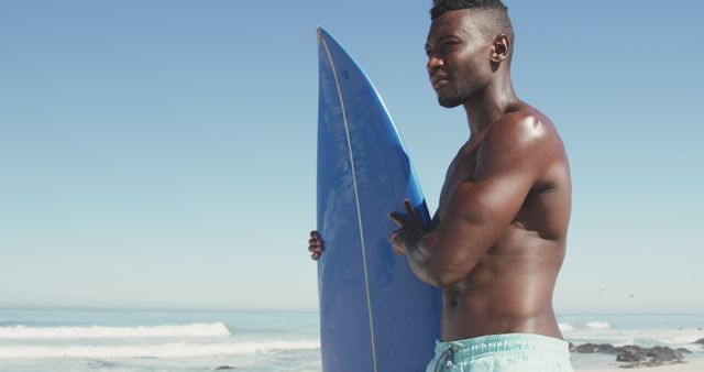 Confident surfer holding blue surfboard on sunny beach - Download Free Stock Images Pikwizard.com