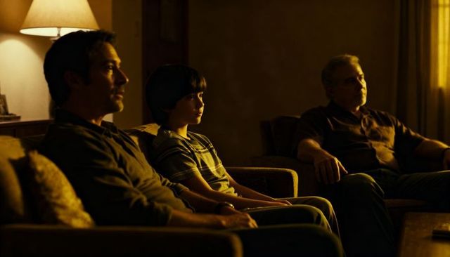 Three-generation family watching tv in cozy living room glowing with warm lamp light