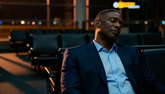 Business traveler sleeping in airport terminal at night wearing navy suit, empty gate