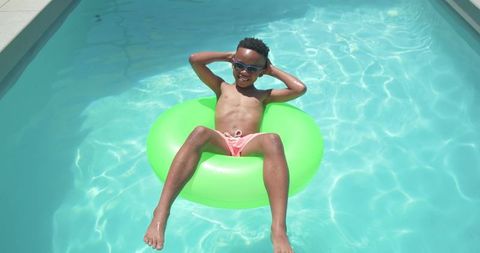 African boy relaxing on neon green float in turquoise pool under bright sun
