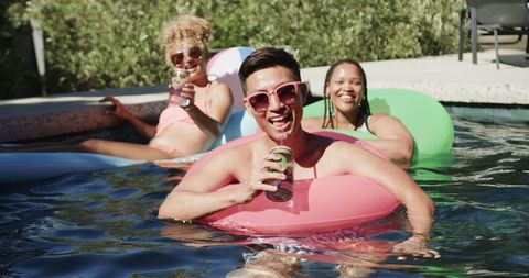 Three friends enjoying drinks and laughing at pool on sunny day
