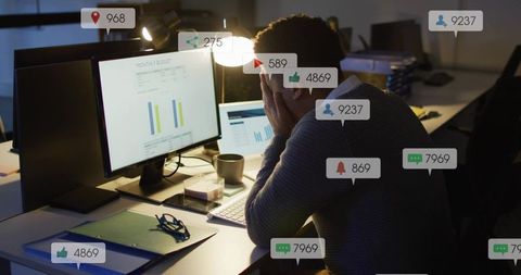 Stressed worker receiving constant notifications while reviewing budget on dim monitors