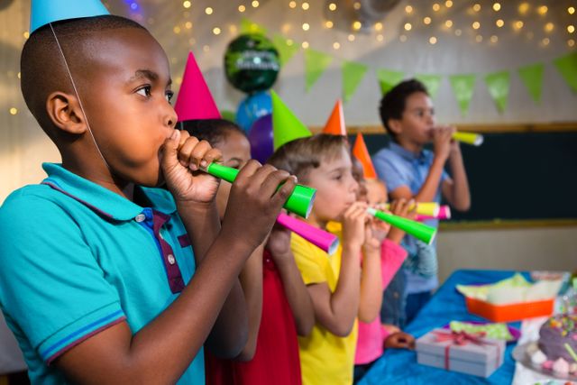 Children blowing party horns while standing by table during birthday party