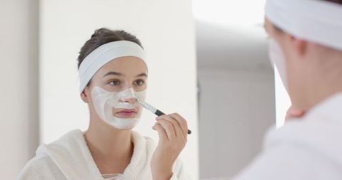 Woman in Bathrobe Applying Facial Mask with Brush in Bathroom