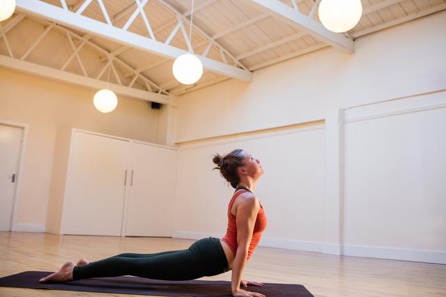 Woman doing cobra pose on exercise mat in fitness studio