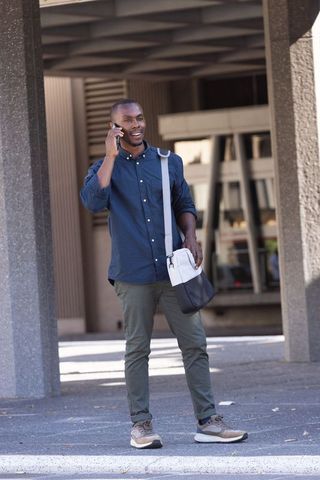 African man talking on phone under urban overhang holding two-tone satchel and smiling