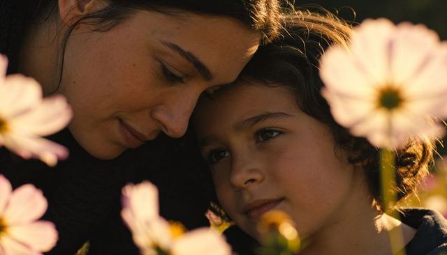 Mother and child cuddling, leaning heads together in wildflower meadow at golden hour