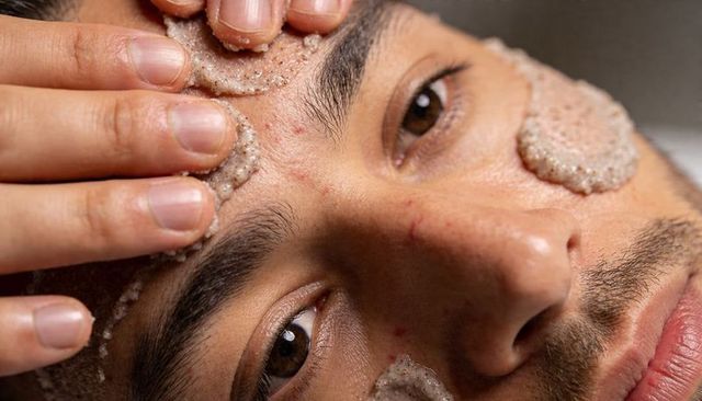 Male face exfoliating closeup applying granular scrub for pore care and skin texture