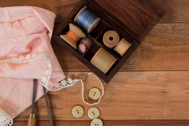 Vintage sewing supplies including thread spools, fabric, buttons, and lace on a wooden table. Ideal for use in crafting blogs, DIY project tutorials, vintage-themed websites, and advertisements for sewing supplies.