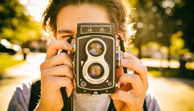Young man holding vintage twin-lens reflex camera adjusting focus in golden hour