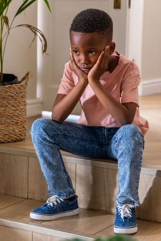 Contemplative african american boy sitting on entry steps cupping face by planter