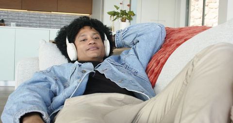 Middle-aged man relaxing on sofa listening to music with headphones in modern living room