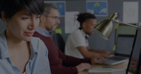 Focused woman typing at laptop in modern open-plan office with collaborative team